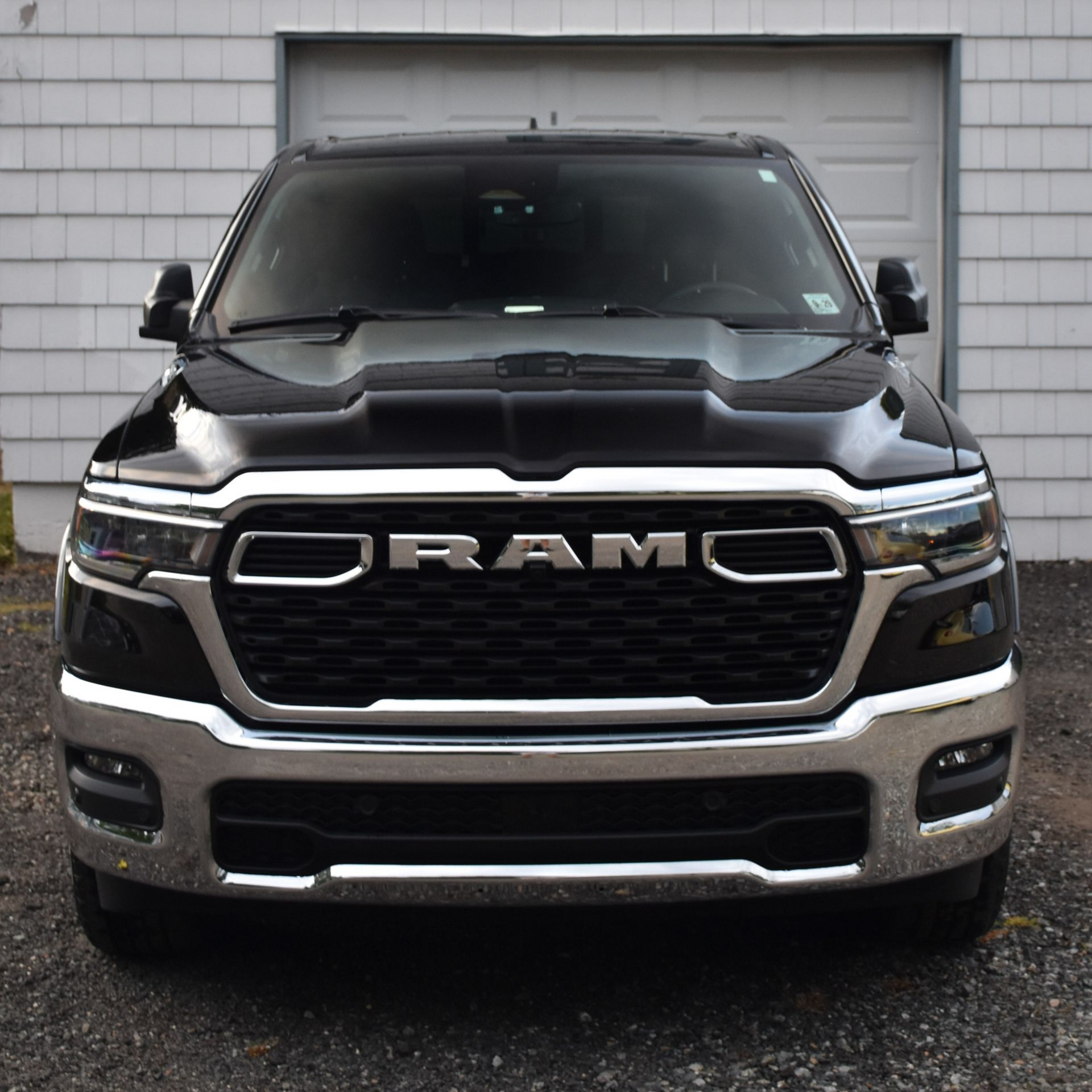 Black Ram truck parked in front of a white building with a gray barn door.