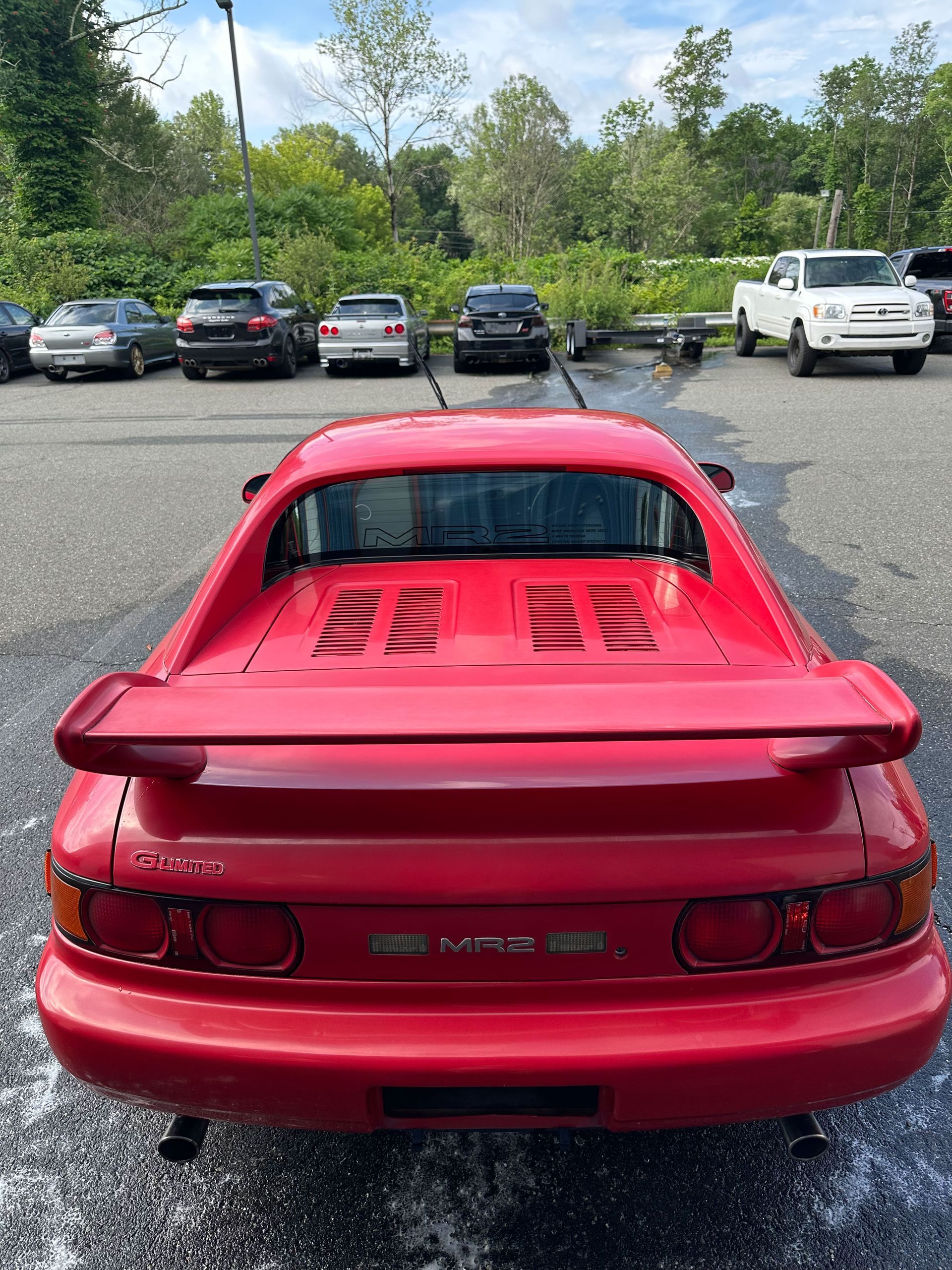 Red Toyota MR2 parked with other cars in a lot. Rear view, spoiler, taillights visible.
