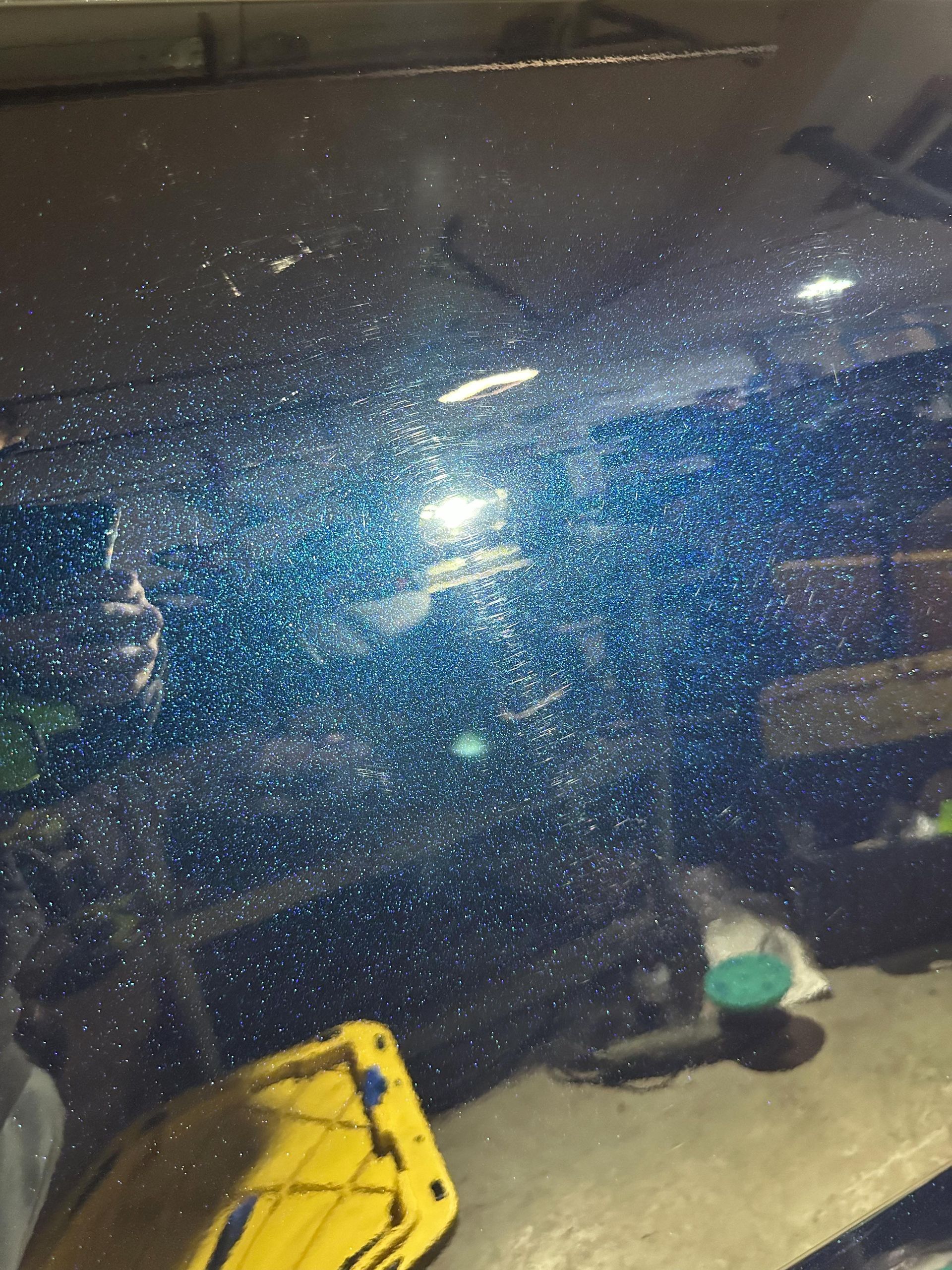 Blue car hood covered in small white reflective specks. Garage setting.