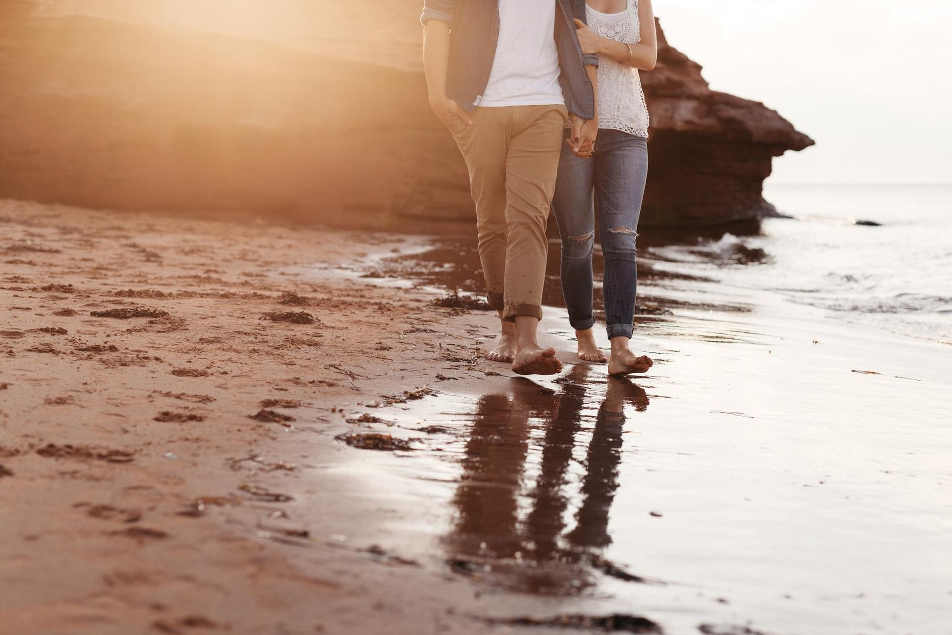 A man and a woman are walking on the beach holding hands.