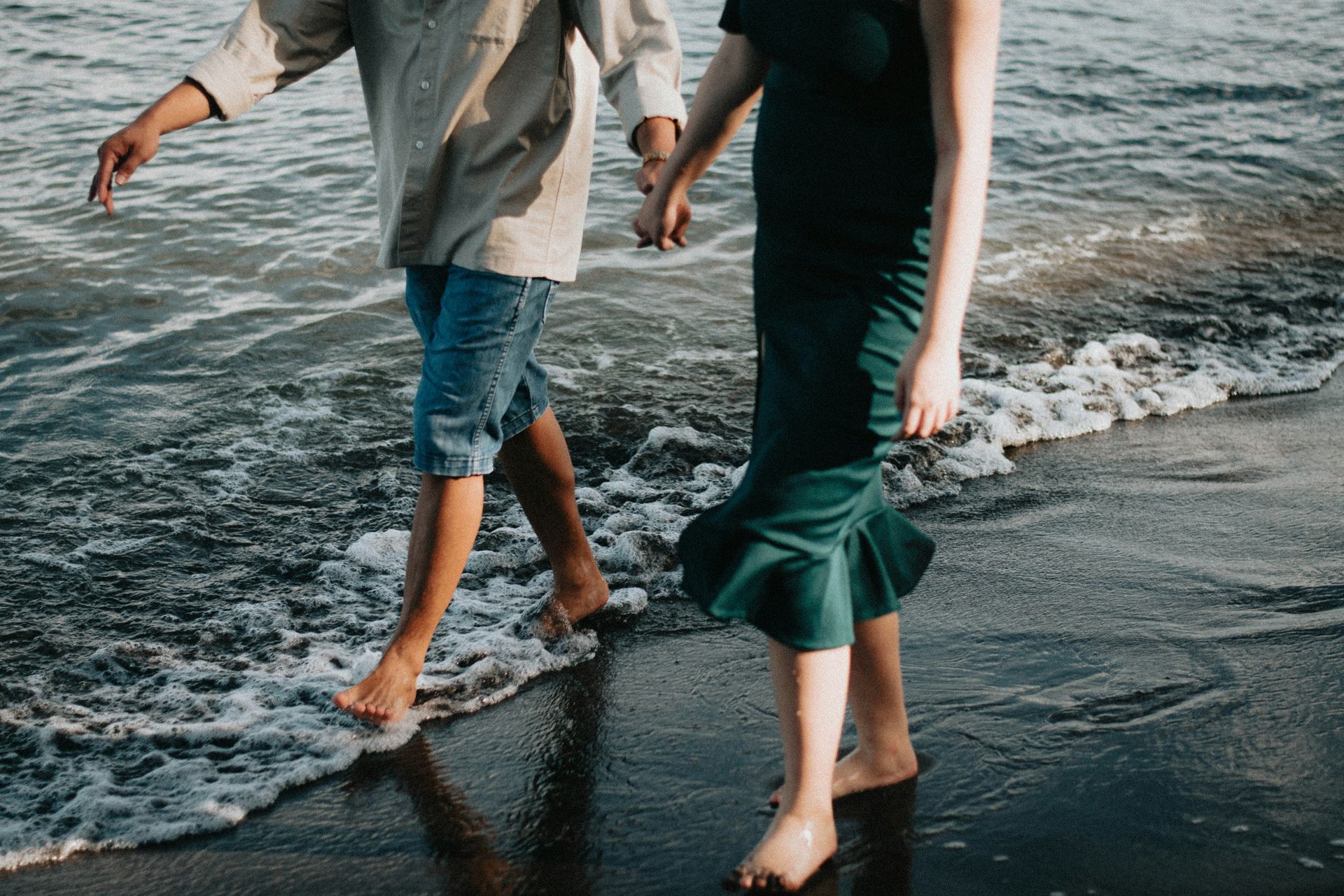 A man and a woman are walking on the beach holding hands.