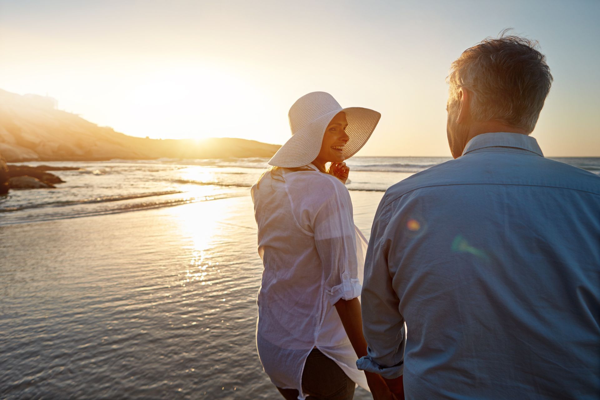 A man and a woman are walking on the beach holding hands.