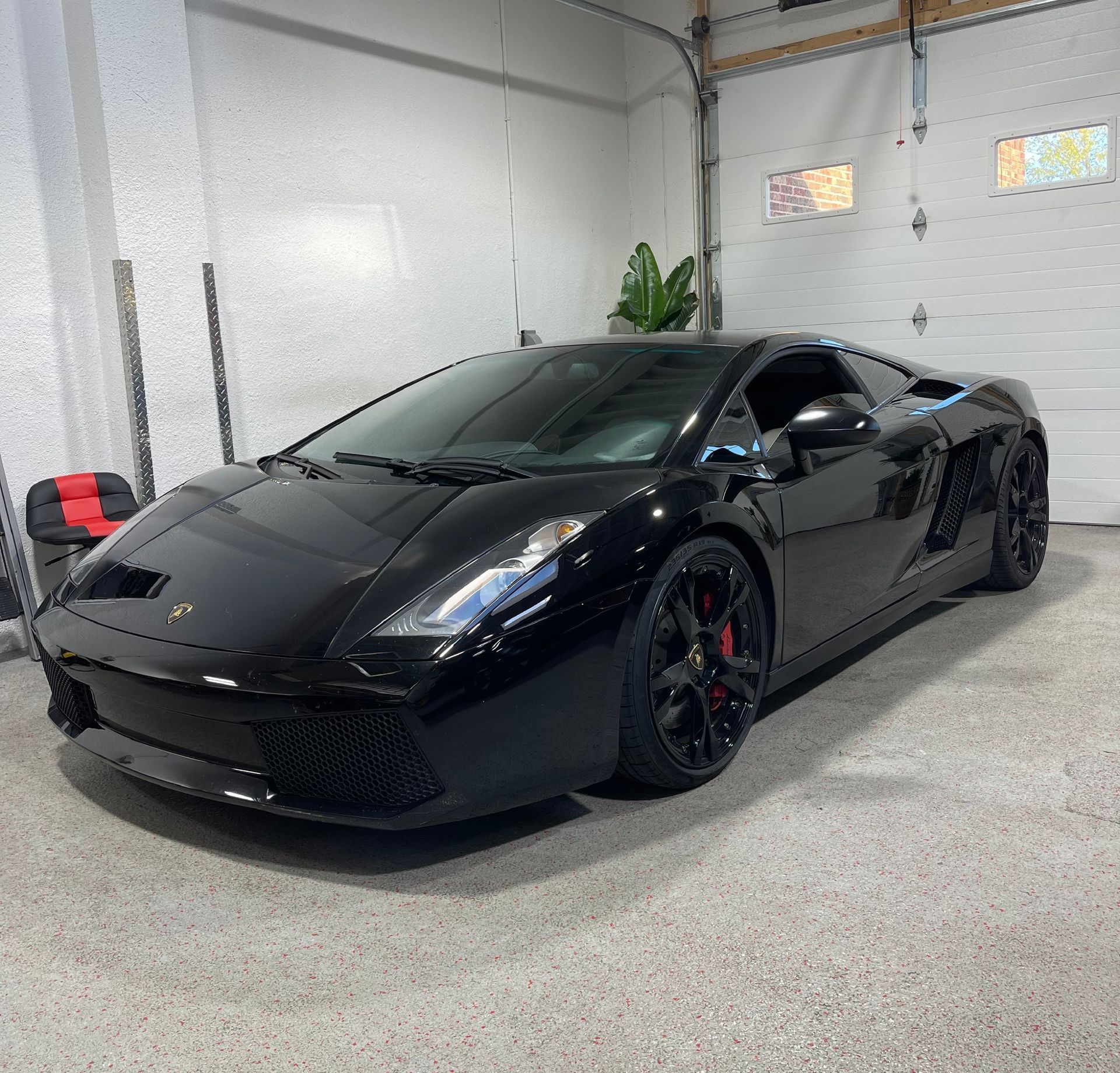 Black Lamborghini sports car parked in a garage with a closed white door.
