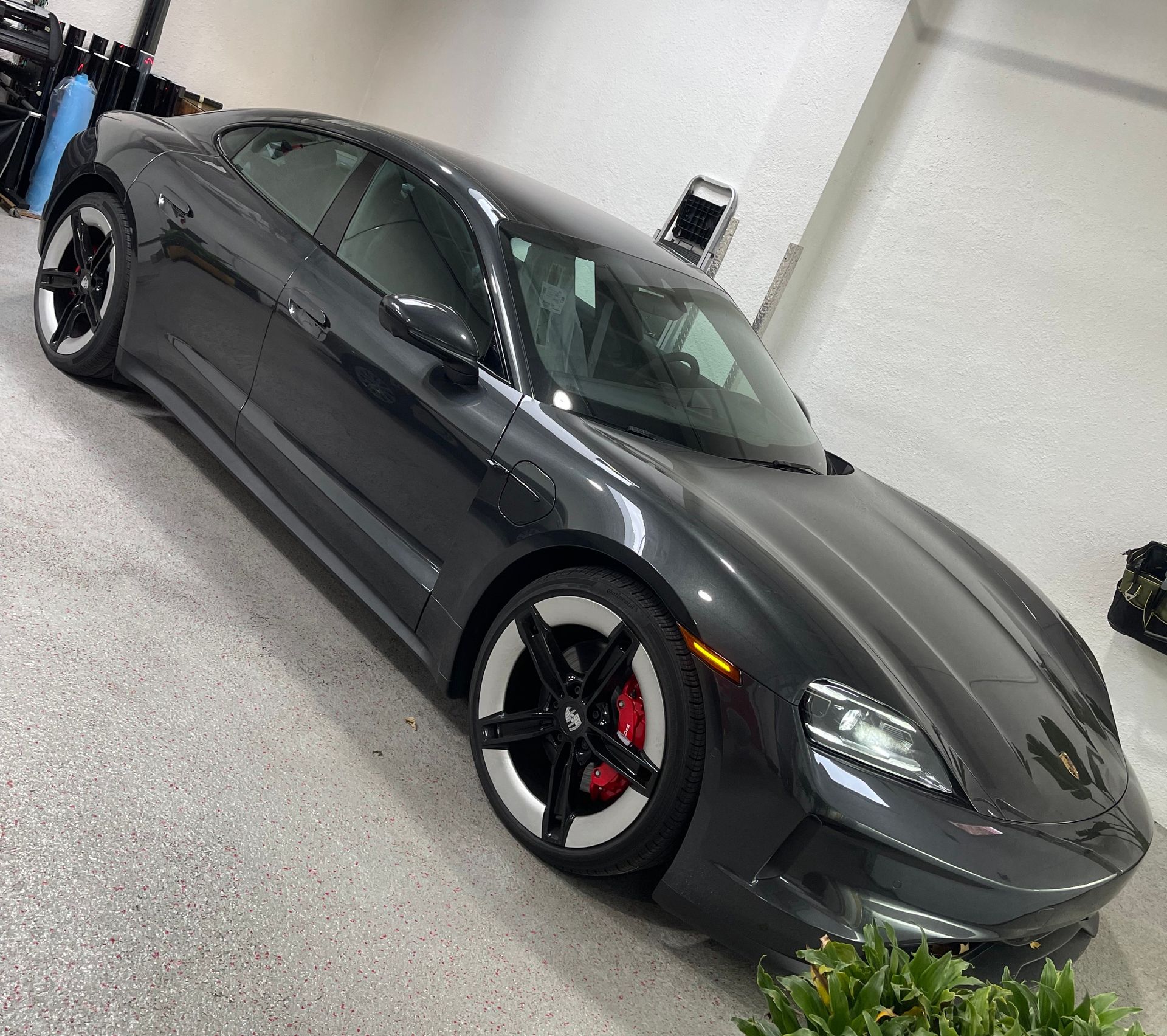 Dark gray Porsche Taycan on a glossy floor, red brake calipers visible, angled view.