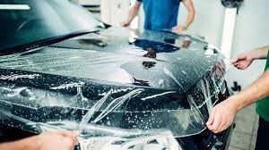 A person applying blue vinyl wrap to a car hood inside a well-lit shop.