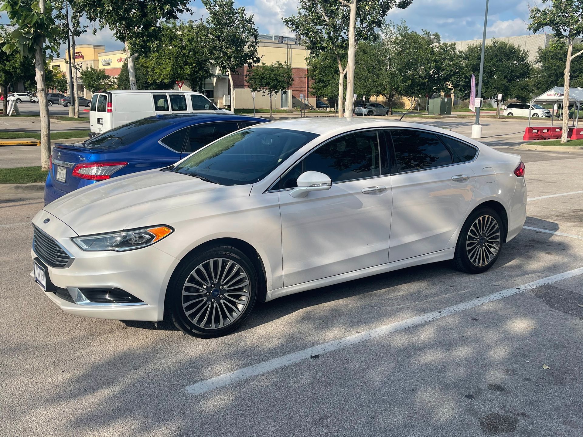 White Ford Fusion parked in a lot; blue car beside it.