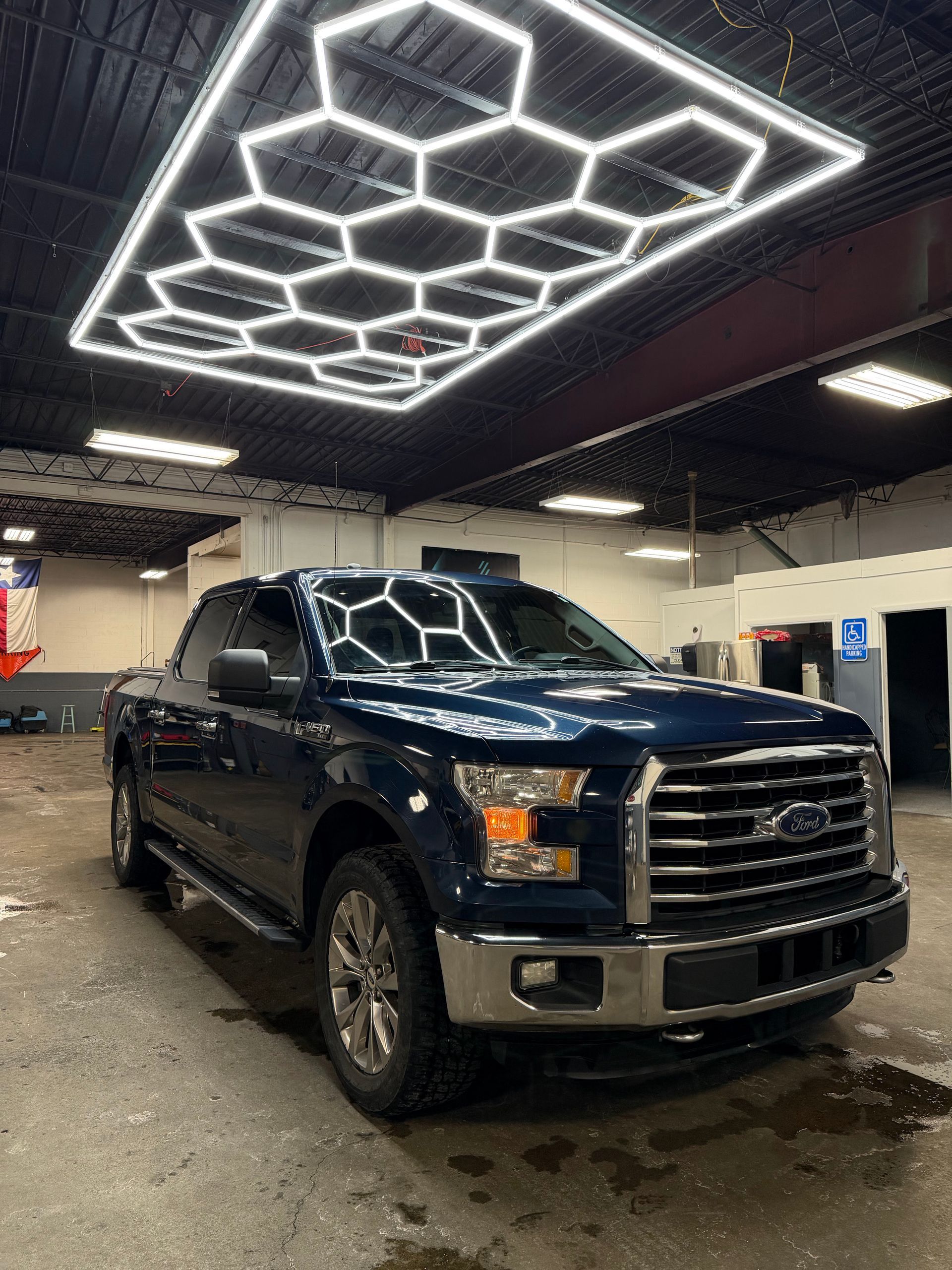 Blue Ford F-150 pickup truck under hexagonal overhead lights in a car detailing bay.