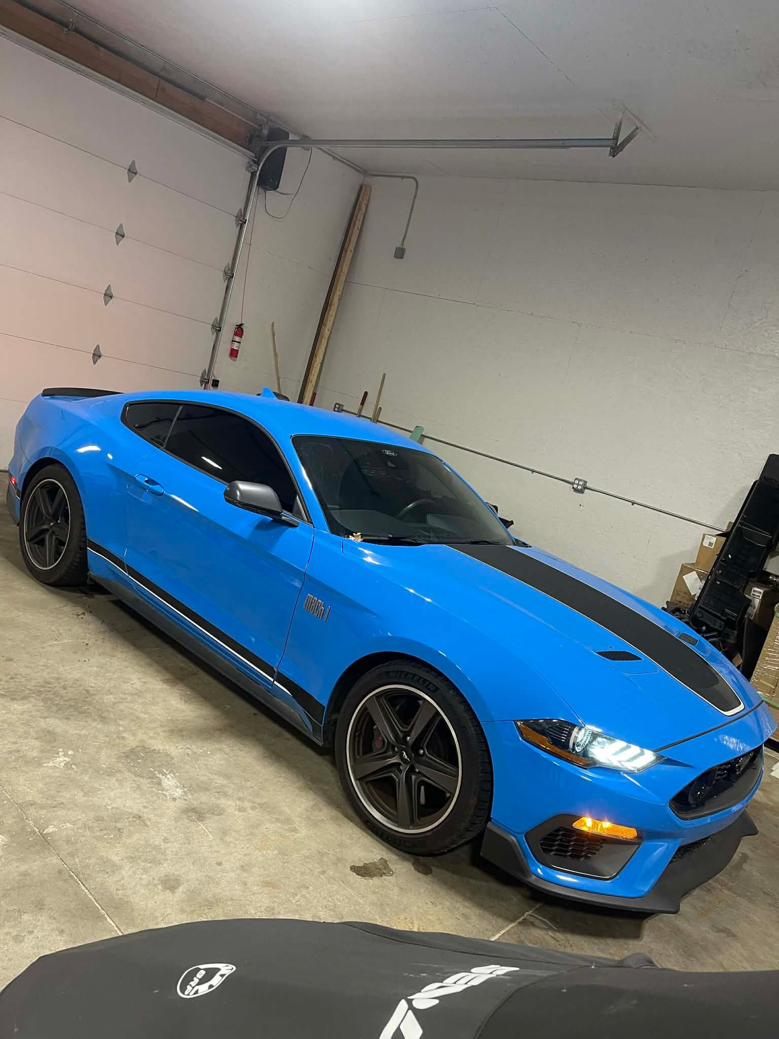 Blue Ford Mustang with black racing stripes parked in a garage.