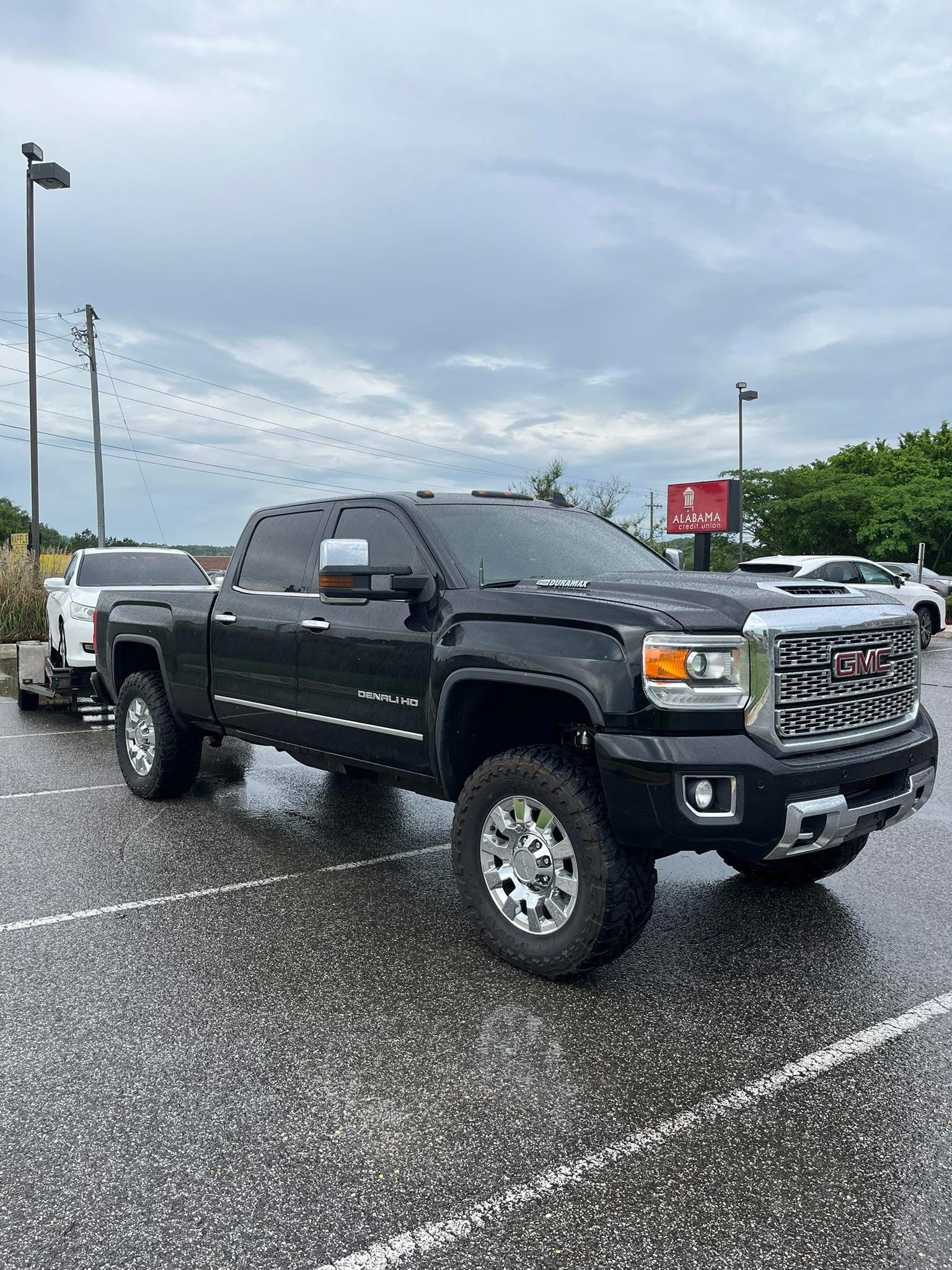 Black GMC Sierra truck parked on a wet lot under a cloudy sky.