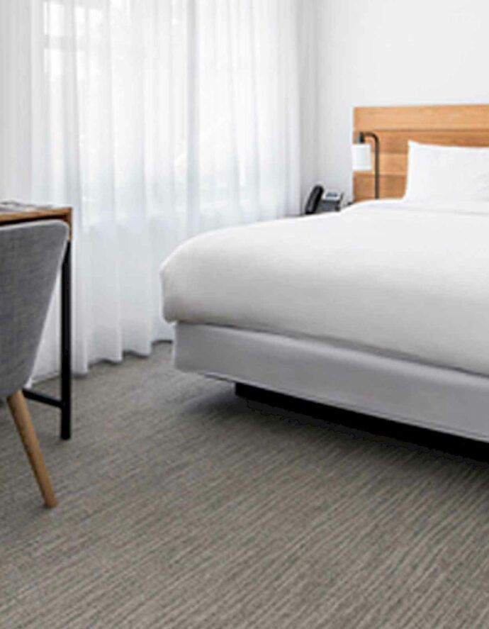 Bedroom with a bed, desk, chair, and window with sheer curtains. Gray carpet.