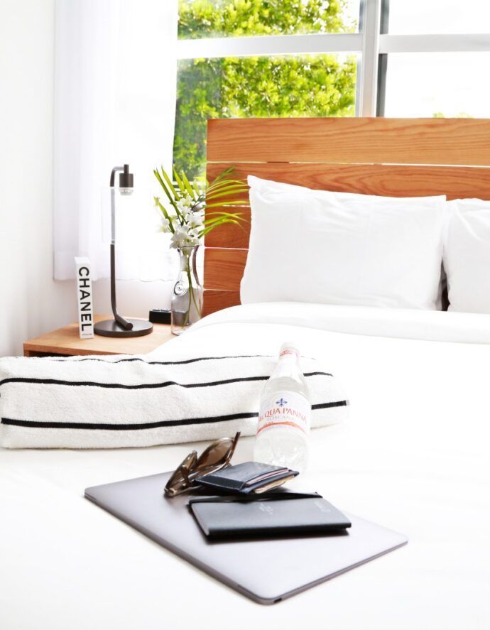 Bedroom with white linens, wooden headboard, laptop, and water bottle.