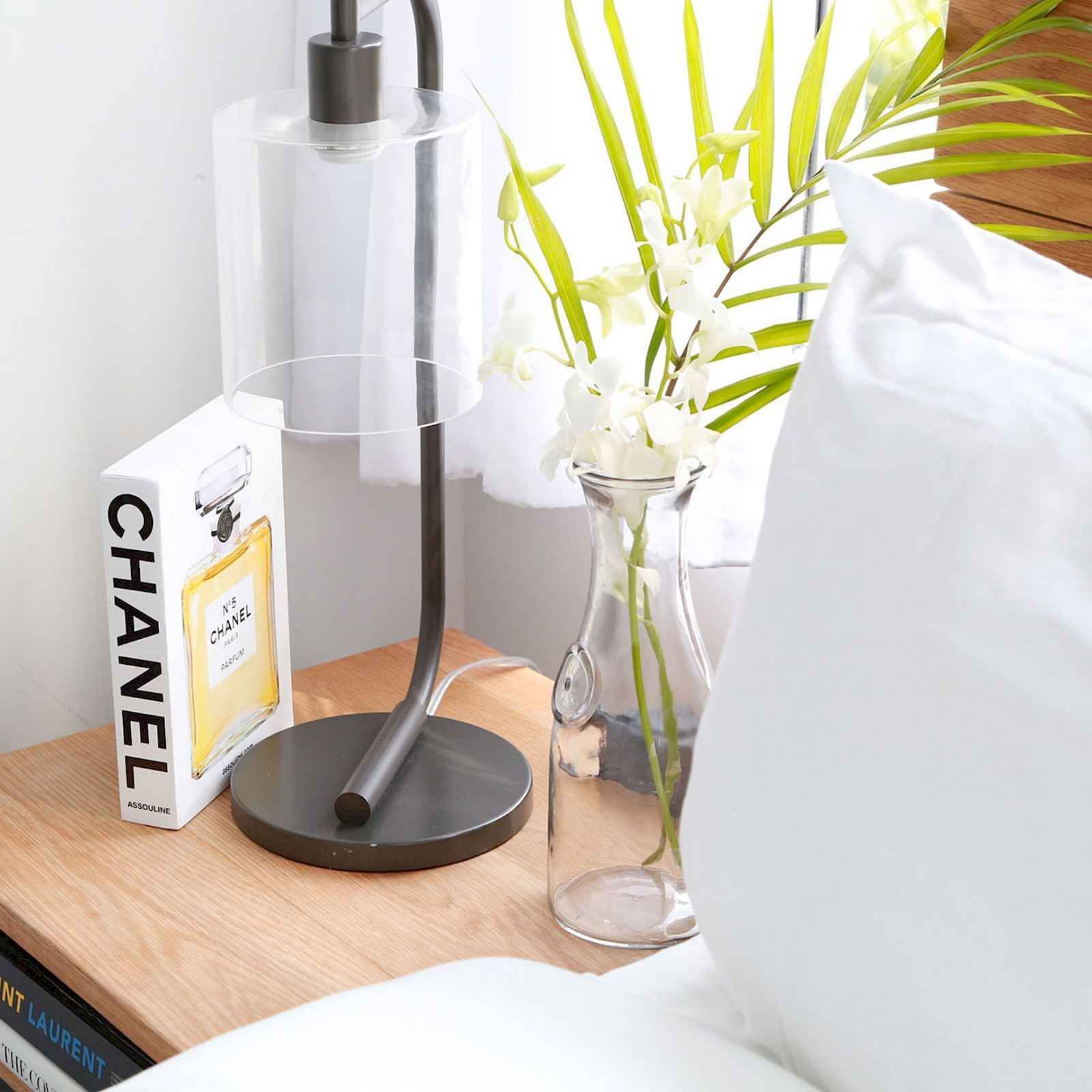 Nightstand with a lamp, a vase of flowers, and a Chanel book.