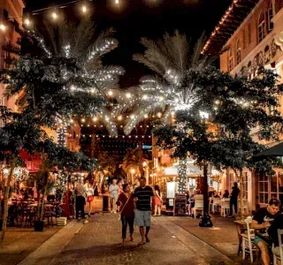 Nighttime street with string lights and people walking past restaurants.