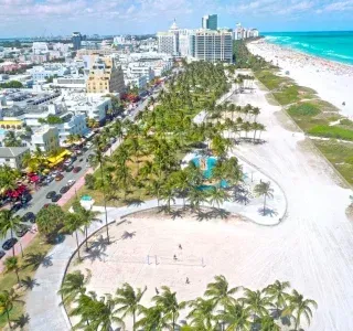 Aerial view of Miami Beach with turquoise water, white sand, palm trees, and buildings.