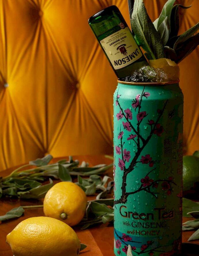Green Arizona Tea can, Jameson bottle, lemon, sage, against a yellow backdrop.