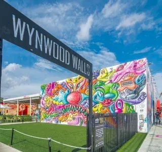 Wynwood Walls sign above vibrant mural art, Miami. Green turf, blue sky, clouds.
