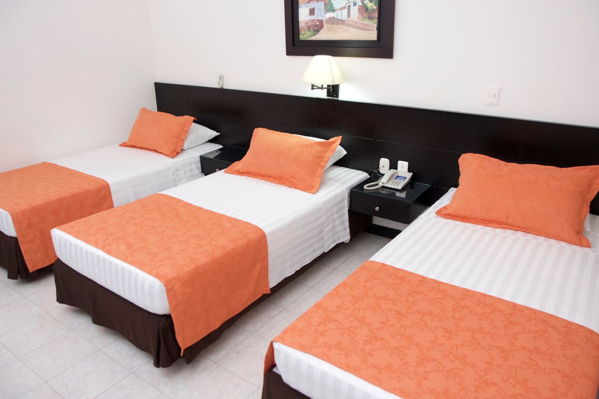 Tres camas en una habitación de hotel con mantas y almohadas naranjas.