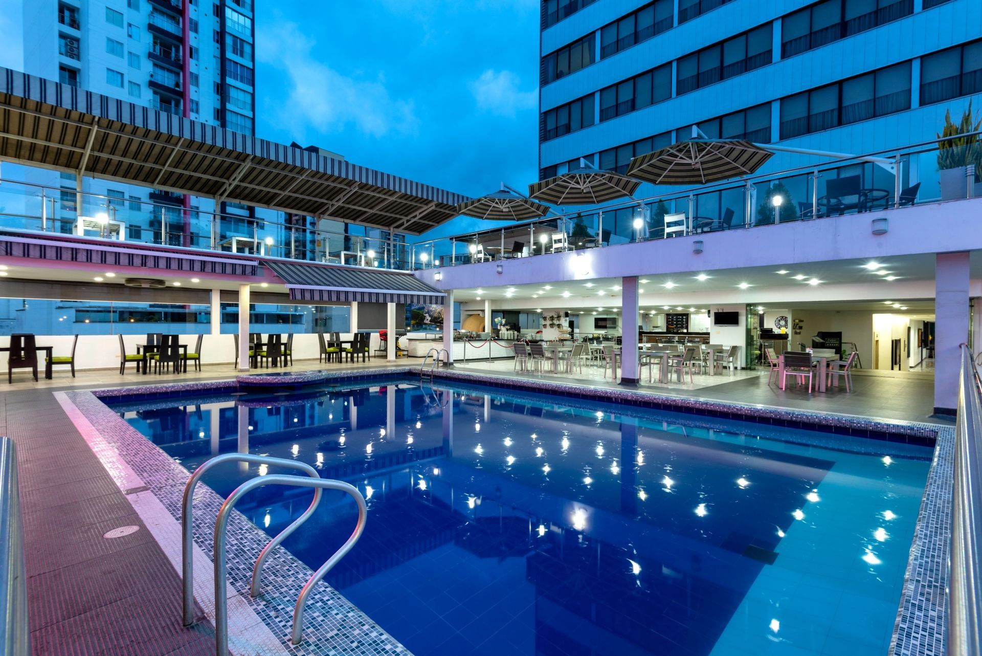 Una gran piscina está rodeada de sillas y sombrillas frente a un edificio.