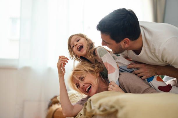 A family of three laughing and playing together on a bed.