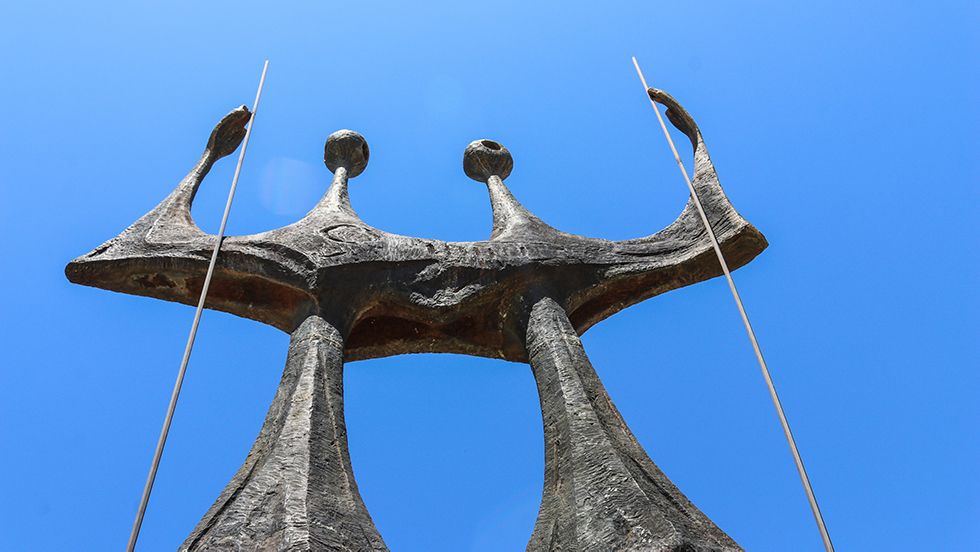 A statue of three people standing next to each other with a blue sky in the background.