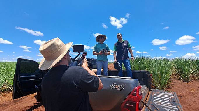 A man is standing in the back of a truck taking a picture of two men in a field.