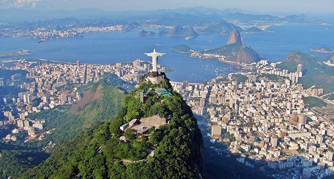 An aerial view of the statue of jesus on top of a mountain overlooking a city.