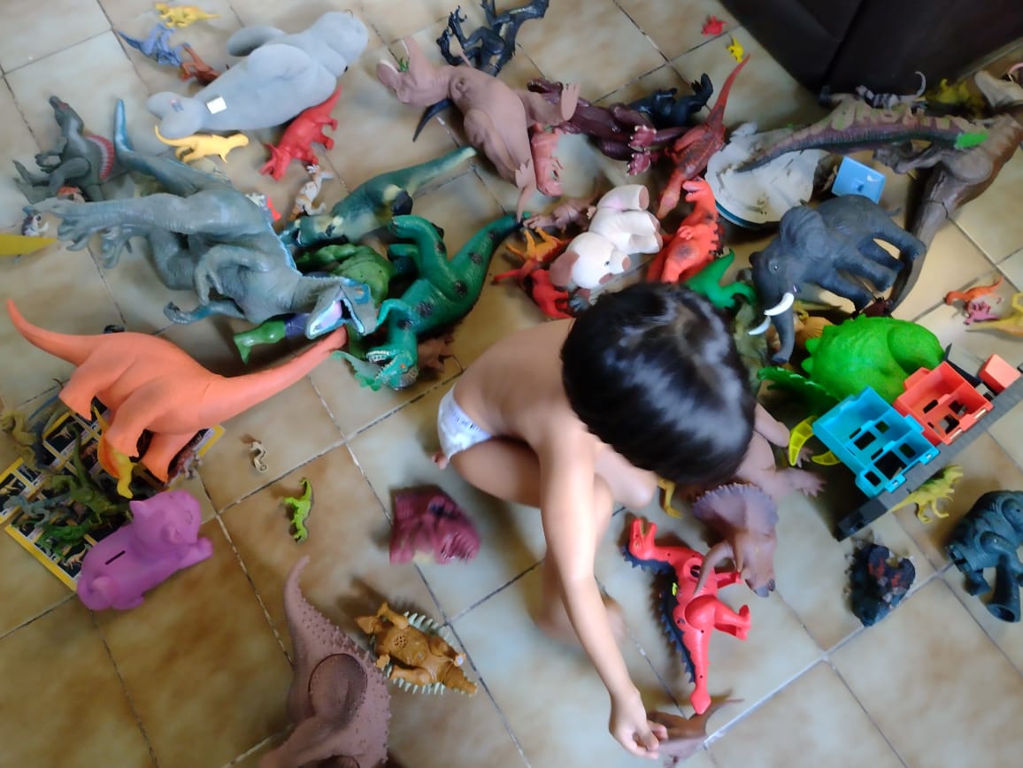 A child is playing with lots of toy dinosaurs on the floor