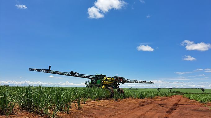A sprayer is spraying a field of corn on a sunny day.