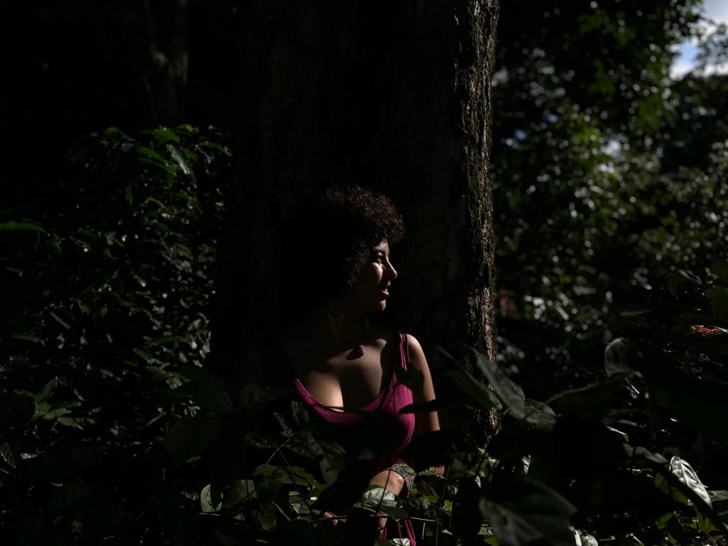 A woman is standing next to a tree in the woods.