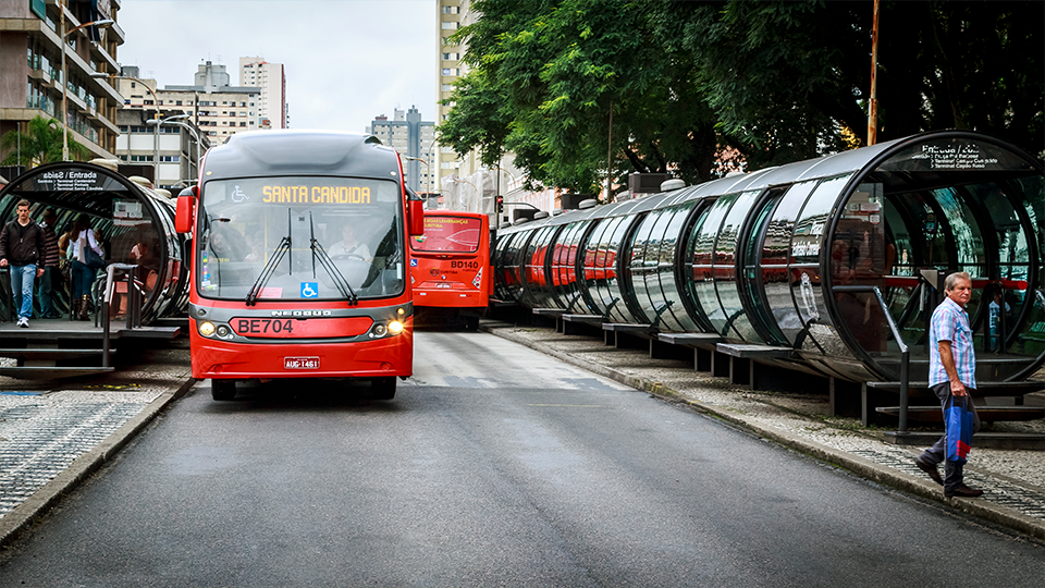 Transporte público A red bus is driving down a city street next to a row of bus stops.