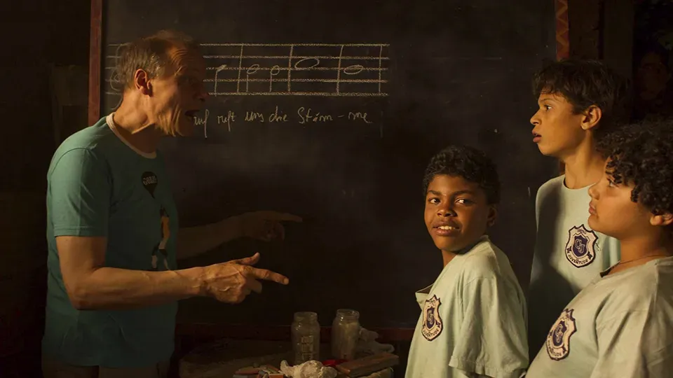 A man is talking to three young boys in front of a blackboard.