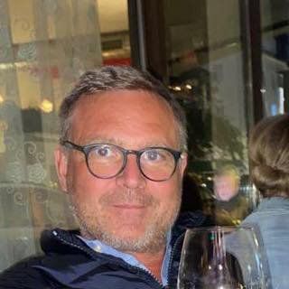 A man with glasses and a beard is holding a glass of wine.