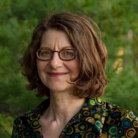 A woman wearing glasses and a colorful shirt is smiling for the camera.