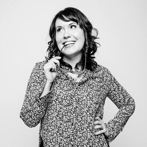 A woman in a floral shirt is holding a pair of glasses in her mouth.