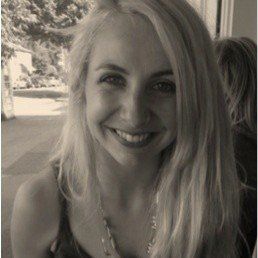 A woman with long blonde hair is smiling in a black and white photo.