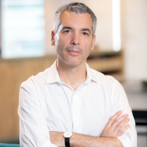 A man wearing a white shirt and a watch is standing with his arms crossed.