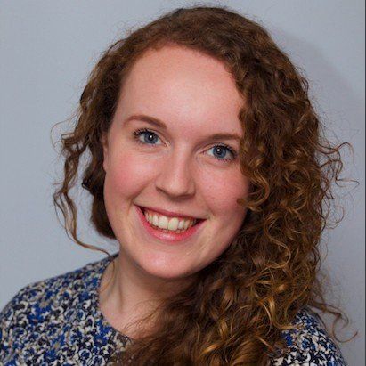 A woman with curly hair and blue eyes is smiling for the camera.