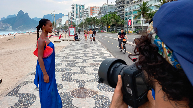 A person is taking a picture of a woman in a blue dress on the beach.