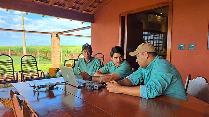 Three men are sitting at a table with a laptop and a drone.