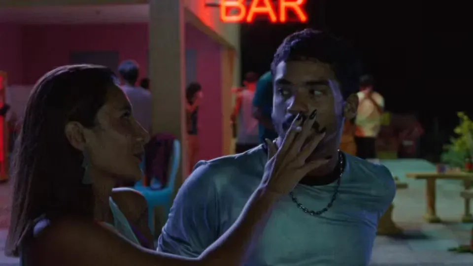 A man and a woman are sitting next to each other in front of a neon sign.