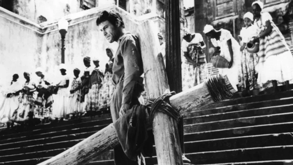 A man is standing on a wooden cross in a black and white photo.