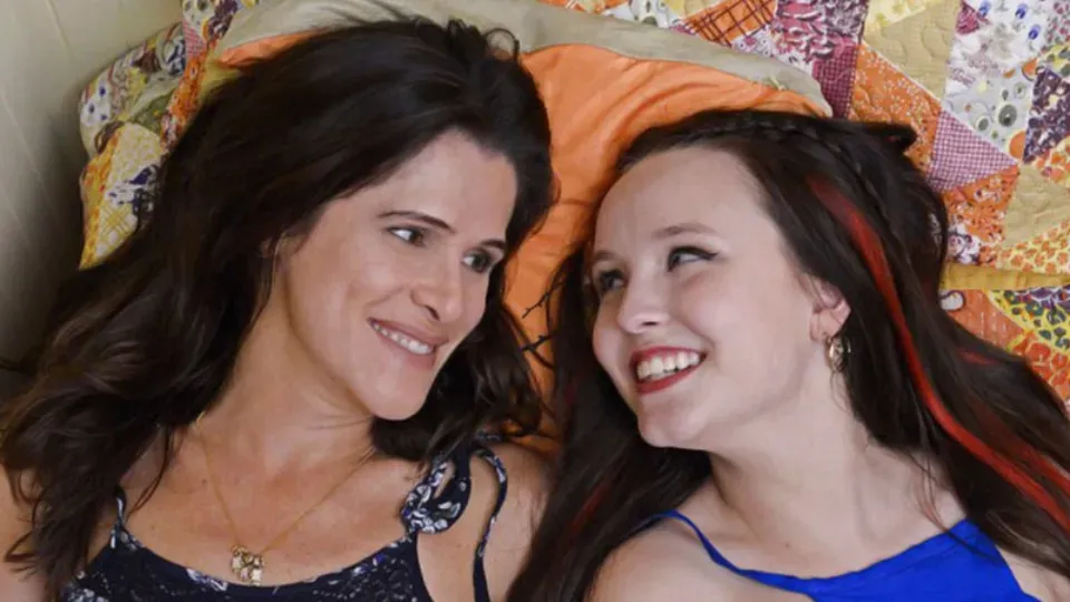 Two women are laying on a bed and smiling at each other.