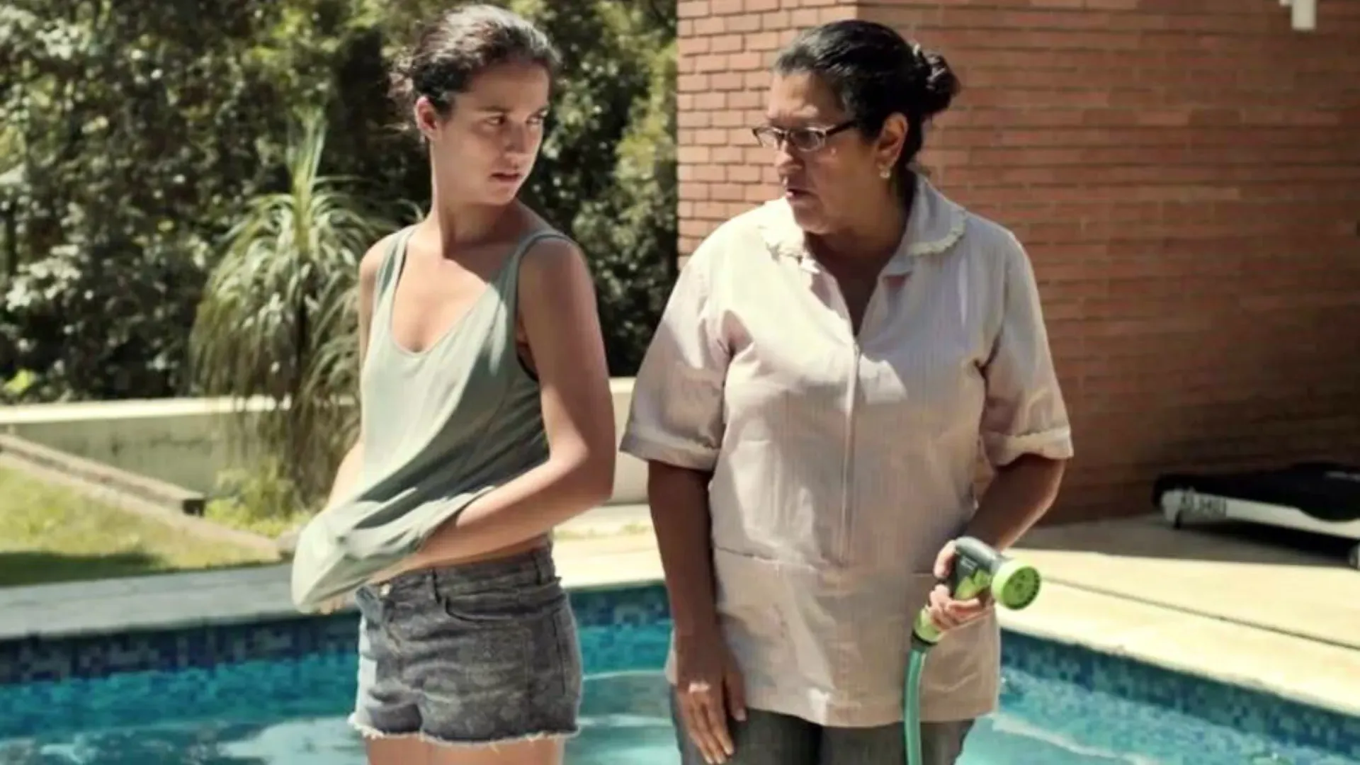 Two women are standing next to a swimming pool.