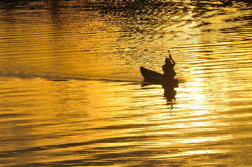 A man is rowing a boat on a lake at sunset.