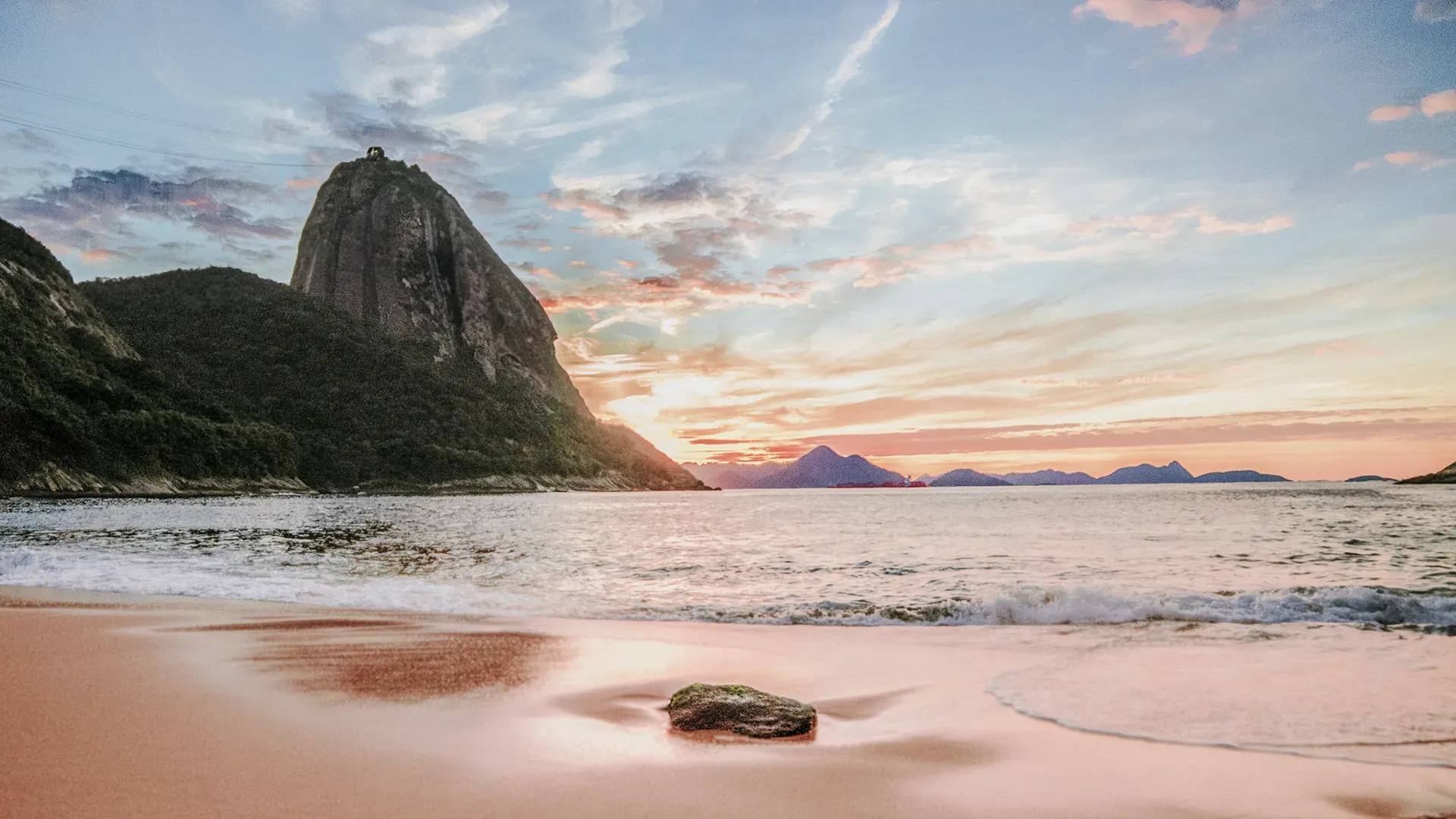 A beach with a mountain in the background at sunset.