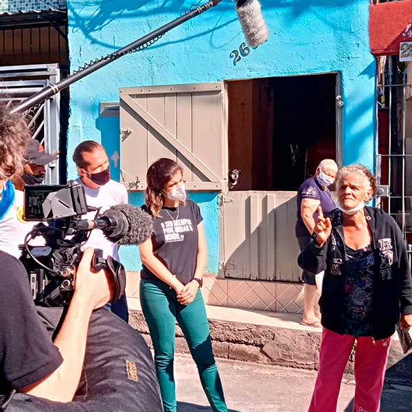 An old woman points at a camera crew while they film