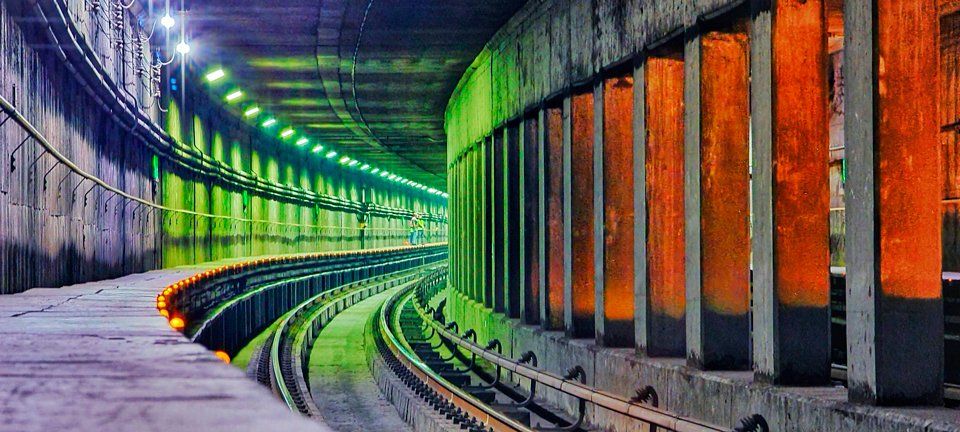 A train track in a tunnel with a fence and lights.