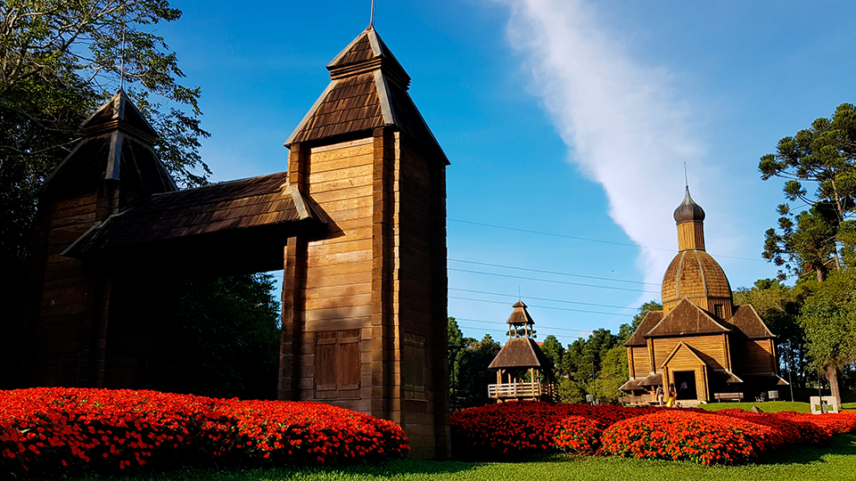 A church and a tower are surrounded by flowers in a park.