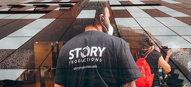 A man wearing a story productions t-shirt is walking down a sidewalk.