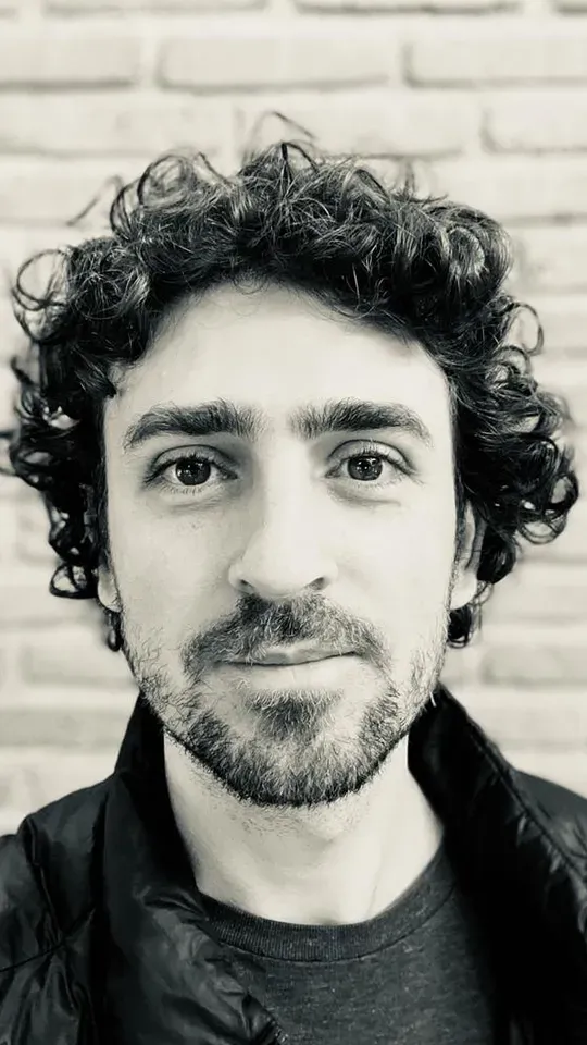 A black and white photo of a man with curly hair and a beard.